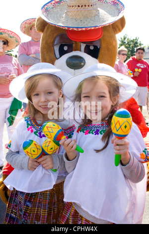 Glückliche junge Mädchen schütteln Maracas mit Bär Maskottchen in die Parade. Mexikanische Unabhängigkeitstag Minneapolis Minnesota MN USA Stockfoto