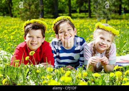 Drei Kinder mit Löwenzahn Kränze, die Erholung auf dem Rasen Stockfoto