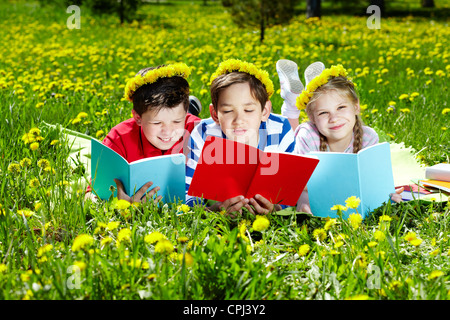 Drei Freunde im Löwenzahn Kränze auf dem Rasen lesen Stockfoto