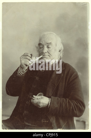 Porträt eines älteren viktorianischen Herrn, der Tabak in eine Tonpfeife aus einem Studio in Liskeard, Cornwall, England, Großbritannien, legt Stockfoto