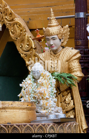 Buddha Figur bedeckt mit Blumengirlanden. Ein Nat, einem buddhistischen Geist in Myanmar verehrt, steht Schutz hinter. Stockfoto