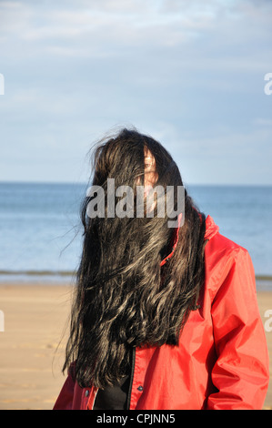 junge Frau am Strand mit langen braunen windgepeitschten Haaren, England, UK Stockfoto