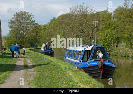 Menschen, die auf einem Schleppweg und schmalen Booten auf dem Leeds Liverpool Canal in der Nähe von Skipton North Yorkshire Dales England Großbritannien Großbritannien Großbritannien Großbritannien Großbritannien Großbritannien Großbritannien Großbritannien Großbritannien Großbritannien Großbritannien und Nordirland wandern Stockfoto