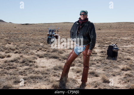 Ältere Mann mit Sonnenbrille, Lederchaps und eine Jacke, die mitten in der Wüste mit seinem Motorrad und Pack abheben. Stockfoto