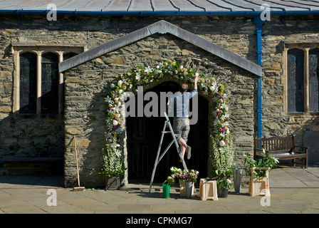 Junger Mann, die Dekoration der Veranda des St.-Martins Kirche für eine Hochzeit, Bowness, Nationalpark Lake District, Cumbria, England Stockfoto