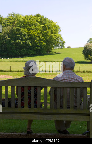 Älteres Ehepaar entspannend auf Bank im Feld im Dorf Chawton, Hampshire, UK. Stockfoto