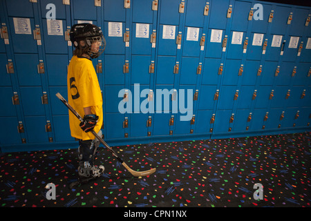 Neun Jahre alten Jungen für Rollhockey stehen vor einer Wand blaue Schließfächer gekleidet. Stockfoto