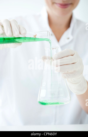 Wissenschaftler Gießen Flüssigkeit aus Messzylinder in konischen Kolben Stockfoto