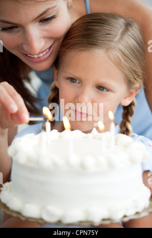 Mädchen beobachten, wie ihre Mutter-Lichter-Kerzen auf Geburtstagskuchen Stockfoto