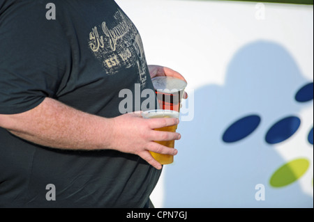 Ein Mann, der Bier in Plastikgläsern im heißen Britischen Sonnenschein mit sich führt Stockfoto