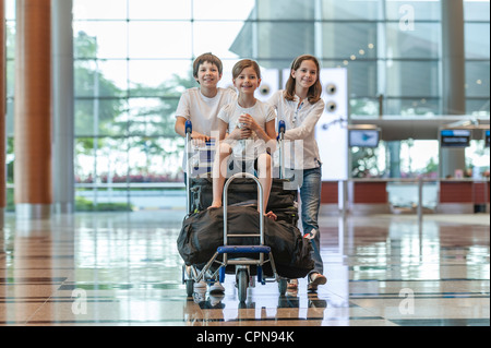 Bruder und Schwester, die jüngere Schwester auf Gepäckwagen am Flughafen schieben Stockfoto