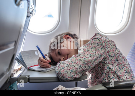 Mädchen auf Tablett-Tisch auf Flugzeug, Kopf ruht in Tagebuch zu schreiben Stockfoto