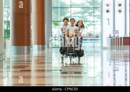 Bruder und Schwester, die jüngere Schwester auf Gepäckwagen am Flughafen schieben Stockfoto