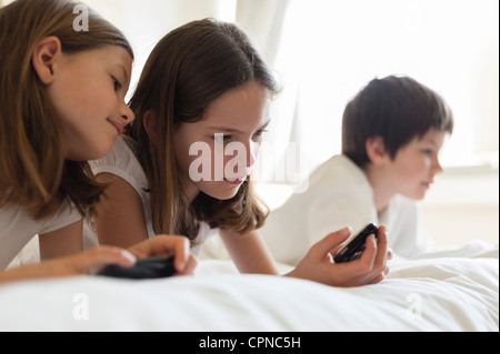 Schwestern auf Bett Videospiel handheld, junge im Hintergrund Stockfoto