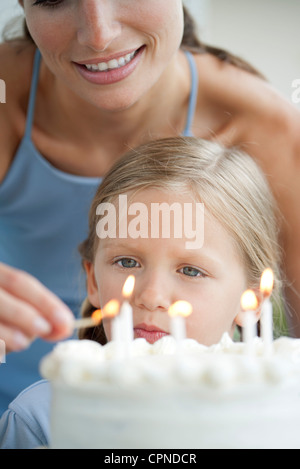 Mädchen beobachten, wie ihre Mutter-Lichter-Kerzen auf Geburtstagskuchen Stockfoto