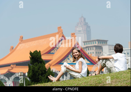 Mädchen sitzen auf dem Rasen mit Bruder in der Nähe von National Concert Hall, Chiang Kai-Shek Memorial Hall, Taipei, Taiwan Stockfoto