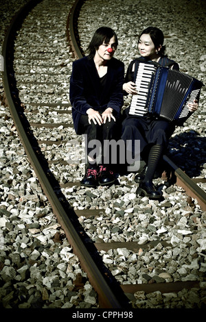 ein Clown paar sitzt auf Eisenbahnschienen, spielt die Frau die Musik Stockfoto