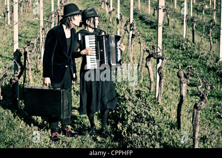 ein Vagabund paar stehend auf einem Feld mit Reben, er hat einen Leder-Koffer, sie spielt auf einem Akkordeon Stockfoto