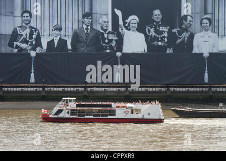 Ein Ausflugsschiff geht vor einem riesigen Foto der Königin und der königlichen Familie winken vom Balkon des Buckingham Palace. Das Bild entstand während der 1977 silbernes Jubiläum und ist montiert auf Container Seehaus an der Themse in London als Teil der 2012 Diamant-Jubiläum feiern. Stockfoto
