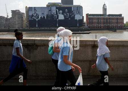 Schulkinder laufen Sie vor einem riesigen Foto der Königin und der königlichen Familie winken vom Balkon des Buckingham Palace. Das Bild entstand während der 1977 silbernes Jubiläum und ist montiert auf Container Seehaus an der Themse in London als Teil der 2012 Diamant-Jubiläum feiern. Stockfoto