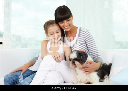 Porträt von fröhliches Mädchen und ihre Mutter kuscheln Shih-Tzu-Hund zu Hause Stockfoto