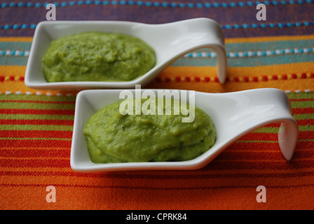 Grüne Bohnen mit Basilikum in Weißware Schale auf bunten Stoff Hintergrund Creme Stockfoto