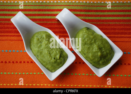 Grüne Bohnen Sahne mit Basilikum in Weißware Schale auf orange Stoff Hintergrund Stockfoto