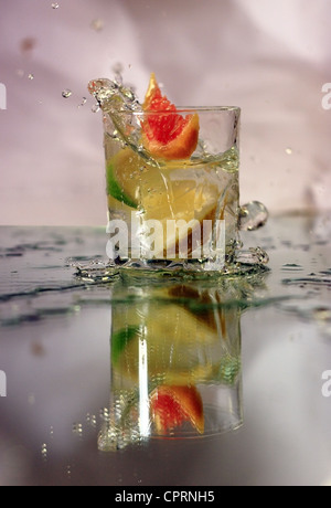 Eine Scheibe Zitrone, Limette und Grapefruit in ein Glas Wasser auf einem Spiegel reflektiert die Spash gefallen wird. Stockfoto