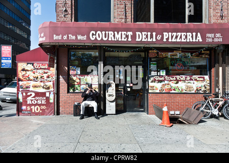 Alter Mann sitzt auf einer Kiste vor typischen New York Ecke Deli an schönen Tag rauchen & reden auf seinem Handy Manhattan Stockfoto