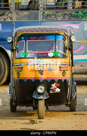 Schwarz-gelbes Auto Rikscha Kopf auf vor einen Bus in Indien Stockfoto