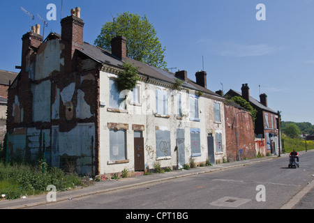 Ein Mann auf einem Elektromobil fährt vorbei an einer Reihe von Lauf nach unten und verlassenen verfallene Häusern in Sheffield, South Yorkshire, England Stockfoto