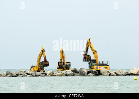 Ein Trio von Aushubmaschinen, die ein künstliches Riff bauen, Teil der Meeresabwehr für das Dorf Borth, Ceredigion, Wales Stockfoto