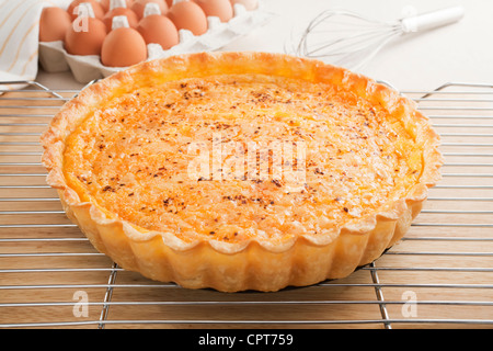 Lachs-Quiche, frisch aus dem Ofen nehmen, abkühlen auf ein Kuchengitter, Eiern und Schneebesen im Hintergrund. Stockfoto