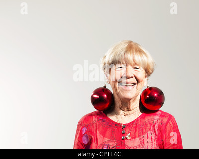 Senior Frau mit roten Kugeln als Ohrringe vor weißem Hintergrund Stockfoto