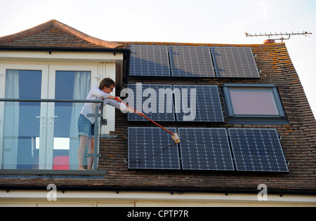 Frau, Reinigung Staub von ihren Solarzellen mit einem Besen auf Dach des inländischen Hause Sussex UK Stockfoto