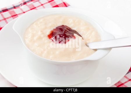 Eine Schüssel mit Milchreis belegt mit Erdbeermarmelade, Löffel im Graben. Stockfoto