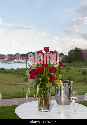 Strauß roter Rosen in Vase auf Terrassentisch mit Weißwein im Hafen Einstellung Stockfoto