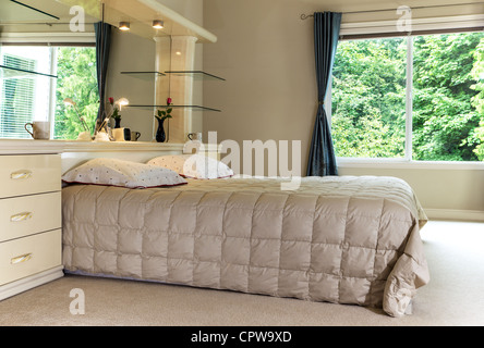 Master-Schlafzimmer mit King size Bett, großer Spiegel und offenen Vorhängen mit grünen Bäumen im Hintergrund Stockfoto