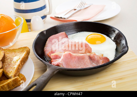 Speck und Ei Frühstück in einer gusseisernen Pfanne erhitzen und einen Teller mit Toast. Stockfoto