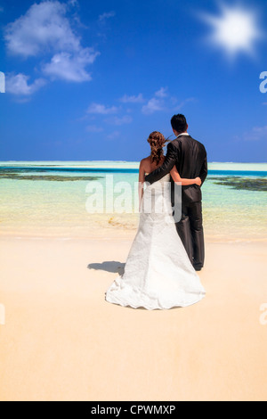 Braut und Bräutigam stehen Arm in Arm die Kamera Blick auf den Ozean auf einem idyllischen tropischen Strand abgewandten Stockfoto