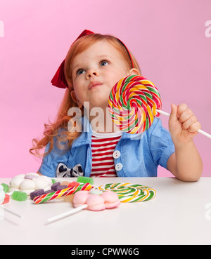 Nachdenklich Mädchen mit Lollipop am Tisch voller Süßigkeiten witting Stockfoto