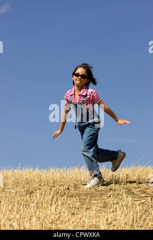 Eine Mädchen überspringt entlang glücklich in einem abgeernteten Weizenfeld. Stockfoto