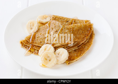 Ein Teller mit Crêpes oder Pfannkuchen mit in Scheiben geschnittenen Banane und Ahornsirup. Stockfoto