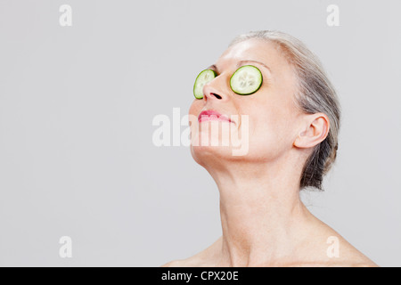 Reife Frau mit Gurkenscheiben über Augen, Lächeln Stockfoto