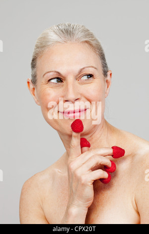 Reife Frau mit Himbeeren auf Fingerspitzen, lächelnd Stockfoto