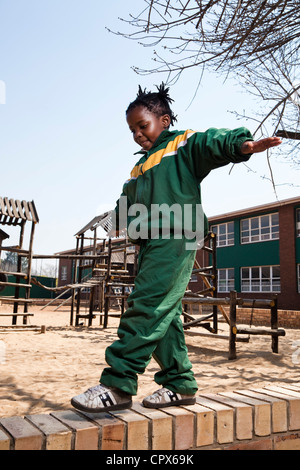 Ein junges Mädchen, das Balancieren auf einer Wand außerhalb Meyerton Primary School, Meyerton, Gauteng Stockfoto