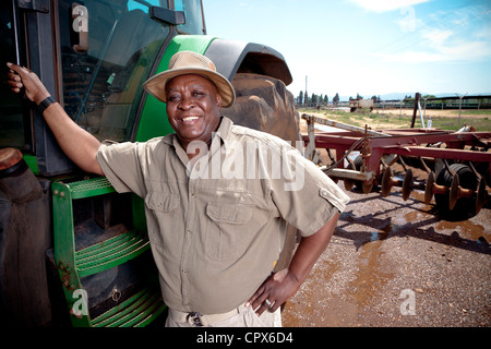 Schwarzer Bauer lehnt sich an einen Traktor und lächelt in die Kamera Stockfoto