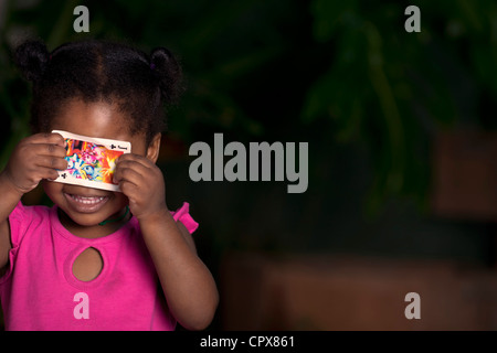 Junge schwarze Mädchen hält eine Spielkarte über ihre Augen Stockfoto