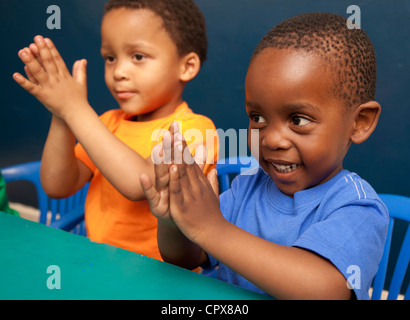 Zwei Kinder sitzen an einem Schreibtisch, klatschten in die Hände Stockfoto