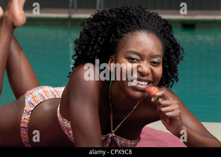 Junge schwarze Frau liegend auf einem Liegestuhl neben einem pool Stockfoto